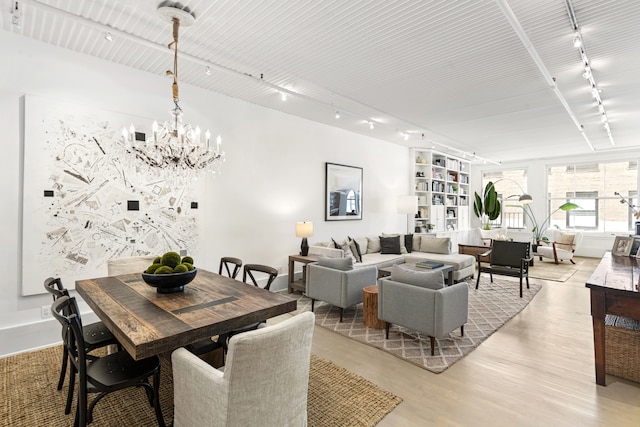 dining space featuring track lighting, light wood-type flooring, and an inviting chandelier