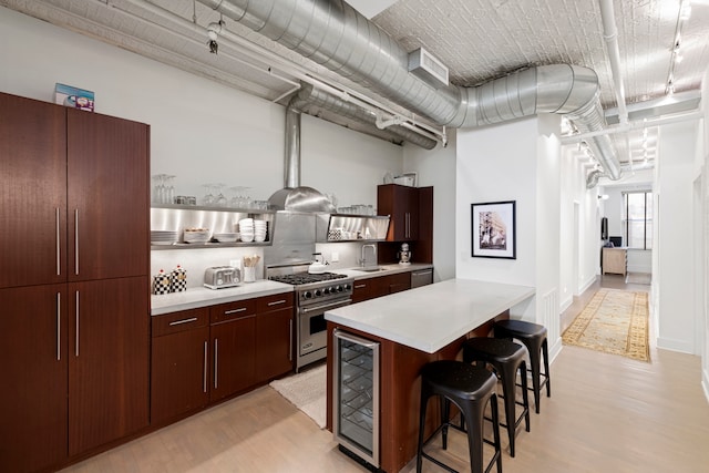 kitchen with sink, light wood-type flooring, a kitchen breakfast bar, stainless steel appliances, and beverage cooler