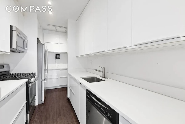 kitchen featuring sink, dark wood-type flooring, rail lighting, white cabinetry, and stainless steel appliances