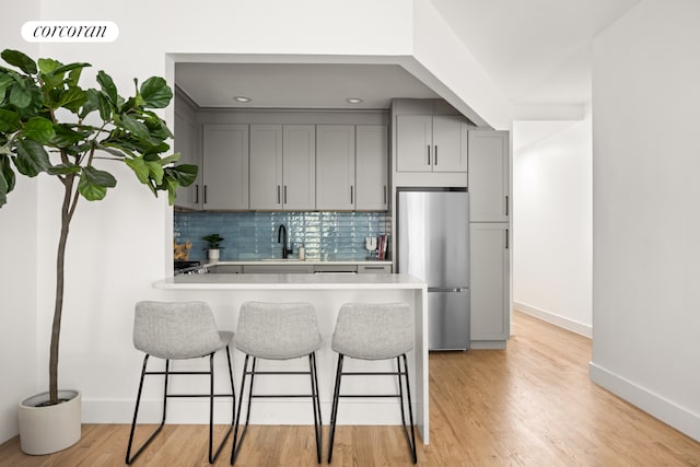 kitchen with stainless steel fridge, kitchen peninsula, tasteful backsplash, gray cabinetry, and light wood-type flooring