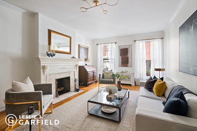 living room featuring radiator, crown molding, light hardwood / wood-style flooring, and a tiled fireplace