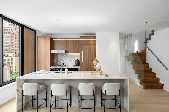 kitchen with light hardwood / wood-style floors, tasteful backsplash, a center island with sink, and a kitchen bar