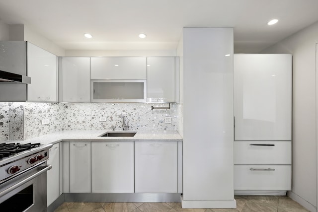 kitchen with high end stainless steel range oven, backsplash, sink, white refrigerator, and white cabinetry