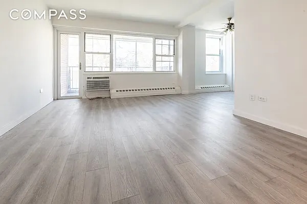 unfurnished living room featuring a baseboard radiator, hardwood / wood-style flooring, and ceiling fan