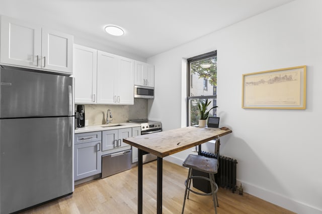 kitchen with tasteful backsplash, appliances with stainless steel finishes, sink, light wood-type flooring, and white cabinetry