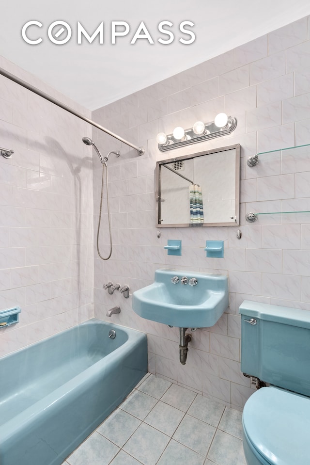 full bathroom featuring toilet, tile patterned flooring, sink, tiled shower / bath combo, and tile walls