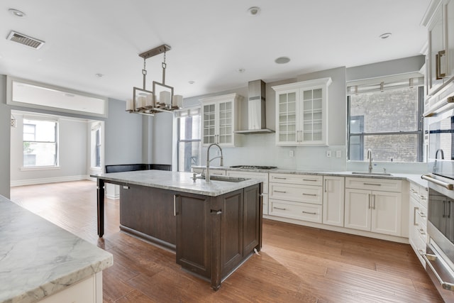 kitchen featuring wood-type flooring, wall chimney exhaust hood, sink, and a center island with sink