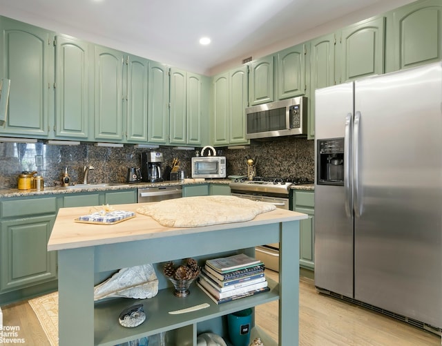 kitchen with stainless steel appliances, tasteful backsplash, light hardwood / wood-style flooring, and green cabinets