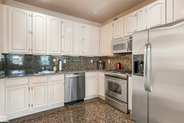 kitchen featuring appliances with stainless steel finishes, white cabinetry, dark stone countertops, and sink