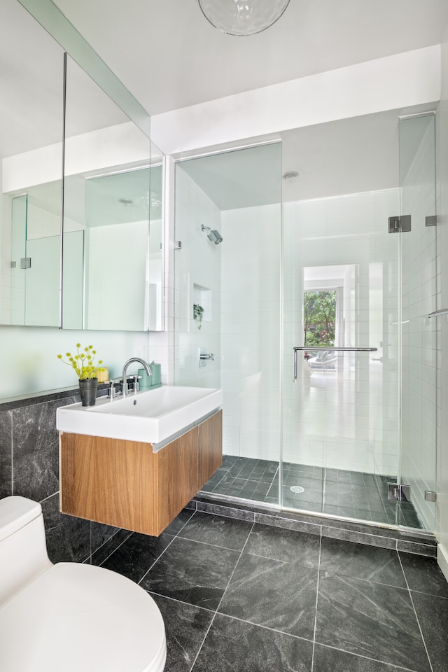 bathroom with vanity, toilet, tile walls, and a shower with shower door