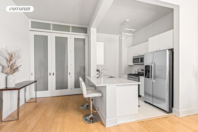 kitchen with a kitchen breakfast bar, stainless steel appliances, sink, light hardwood / wood-style flooring, and white cabinets