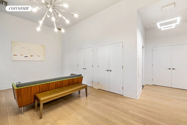 living area featuring a towering ceiling, light hardwood / wood-style floors, and an inviting chandelier