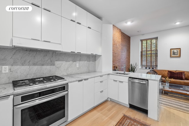 kitchen featuring stainless steel appliances, light stone countertops, kitchen peninsula, and white cabinets