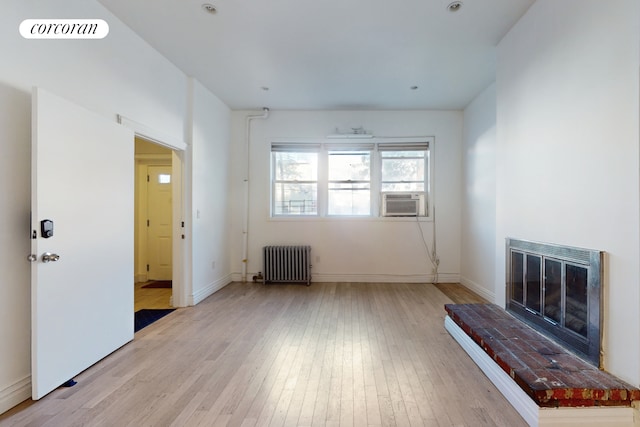 unfurnished living room with radiator, cooling unit, light hardwood / wood-style flooring, and a fireplace