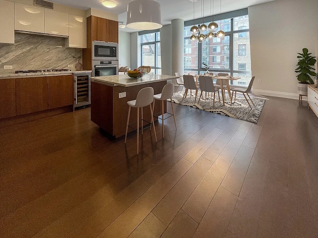 kitchen with a center island, hanging light fixtures, beverage cooler, tasteful backsplash, and appliances with stainless steel finishes