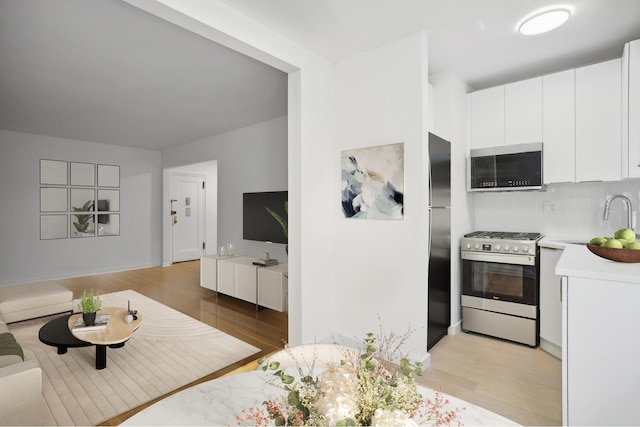 kitchen with sink, white cabinets, light wood-type flooring, appliances with stainless steel finishes, and tasteful backsplash