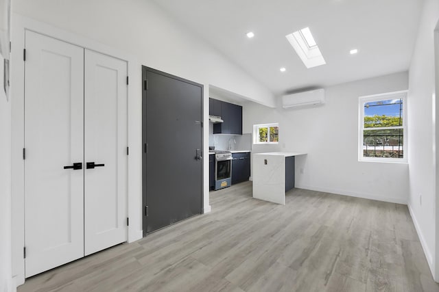 kitchen with vaulted ceiling with skylight, stainless steel range with gas cooktop, an AC wall unit, and light hardwood / wood-style floors