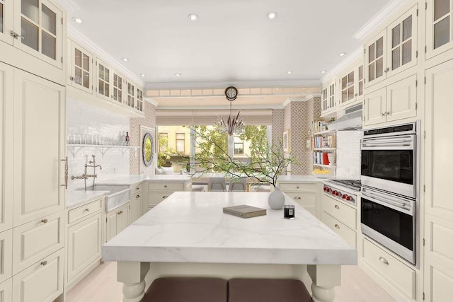 kitchen with decorative backsplash, light stone counters, a kitchen breakfast bar, decorative light fixtures, and sink