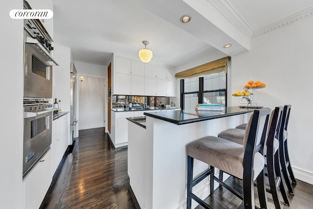 kitchen featuring dark wood-type flooring, oven, a breakfast bar, and white cabinets