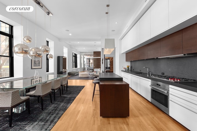 kitchen with dark brown cabinetry, stainless steel appliances, hanging light fixtures, light hardwood / wood-style flooring, and a kitchen island