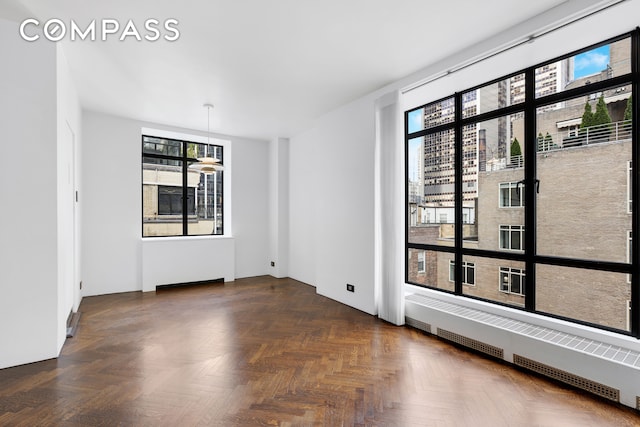 empty room with radiator, plenty of natural light, and dark parquet flooring