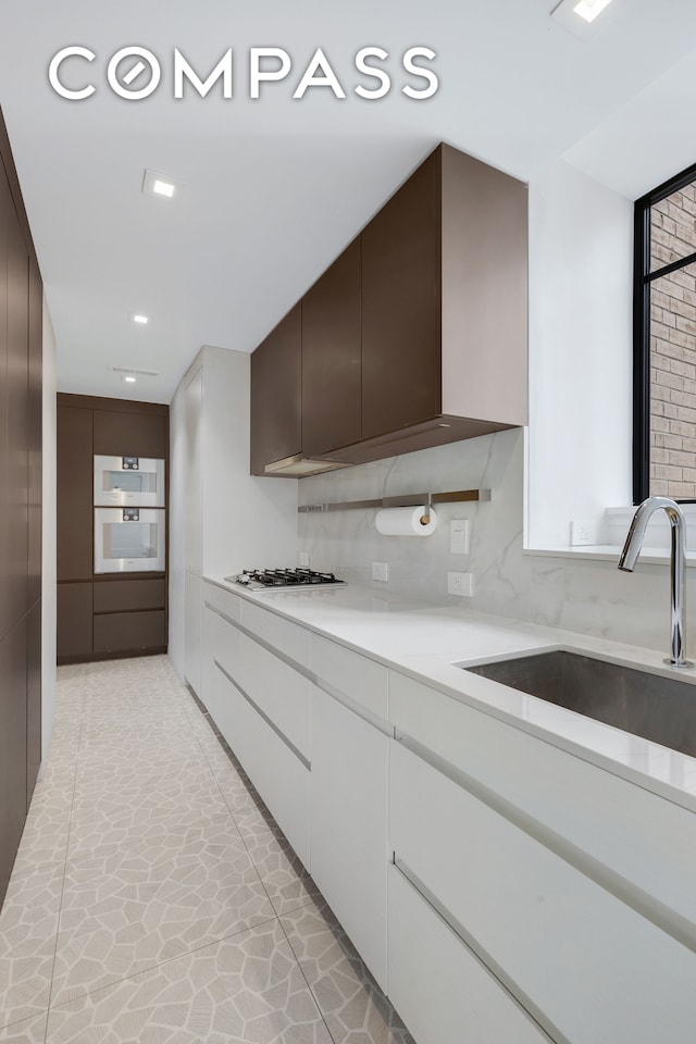 kitchen with sink, backsplash, stainless steel oven, white gas cooktop, and dark brown cabinetry