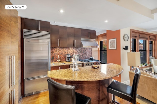 kitchen featuring a kitchen island, extractor fan, stainless steel appliances, light stone counters, and tasteful backsplash