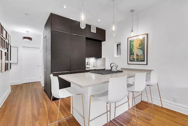 kitchen with light hardwood / wood-style flooring, a kitchen bar, decorative light fixtures, and kitchen peninsula