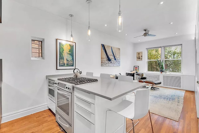 kitchen with high end stove, a kitchen bar, light hardwood / wood-style floors, decorative light fixtures, and white cabinets