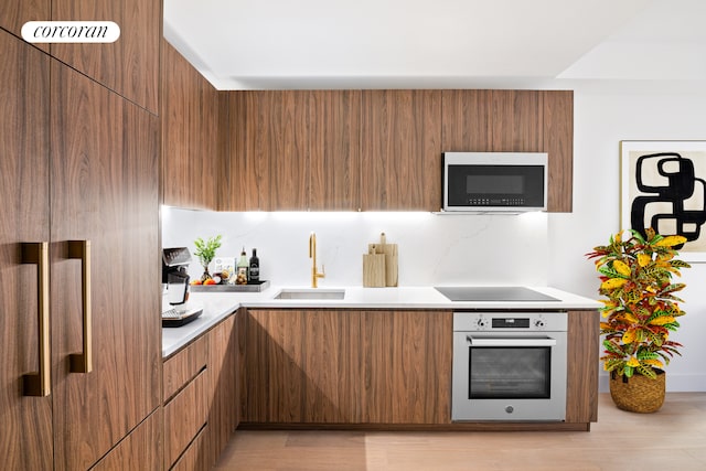 kitchen featuring black electric stovetop, oven, sink, light wood-type flooring, and backsplash