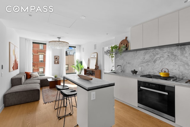 kitchen featuring appliances with stainless steel finishes, decorative backsplash, a kitchen breakfast bar, white cabinets, and light hardwood / wood-style flooring