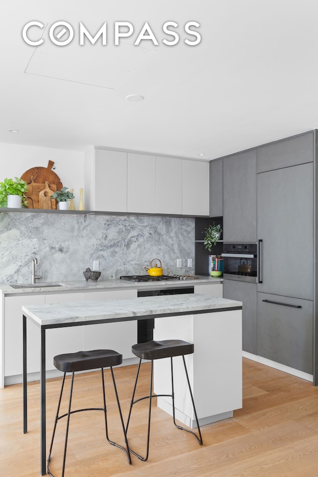 kitchen with light wood-type flooring, gray cabinets, sink, a kitchen breakfast bar, and a center island