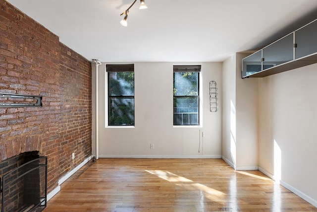 unfurnished living room with light hardwood / wood-style flooring, brick wall, and a brick fireplace