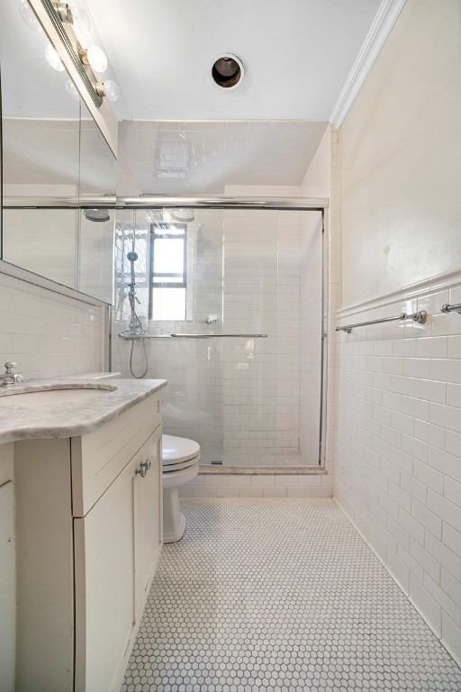 bathroom with an enclosed shower, vanity, crown molding, tile walls, and tile patterned flooring