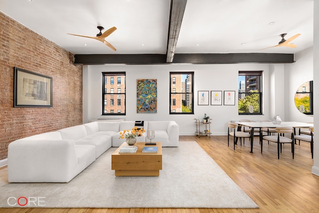 living room with ceiling fan, brick wall, beamed ceiling, and light wood-type flooring