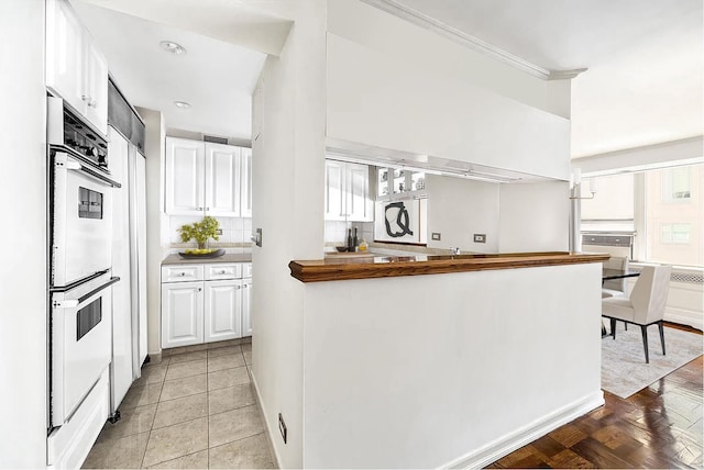 kitchen with white cabinets, white double oven, light tile patterned floors, and backsplash