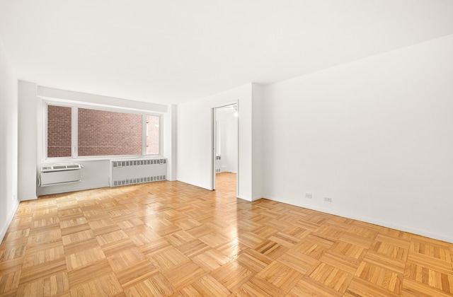 spare room with a wall mounted AC, radiator heating unit, and light parquet flooring