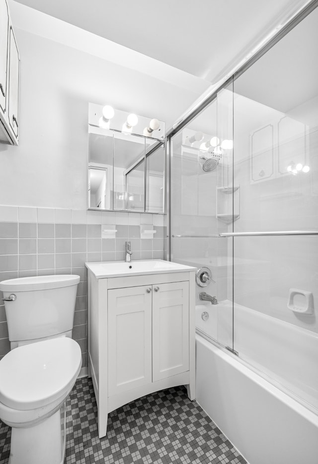 full bathroom with tile walls, vanity, bath / shower combo with glass door, and toilet