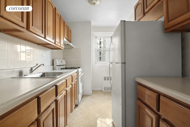 kitchen featuring white appliances, tasteful backsplash, sink, radiator heating unit, and light tile patterned floors