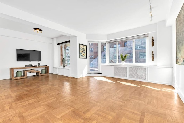 unfurnished living room featuring light parquet flooring, rail lighting, and a healthy amount of sunlight