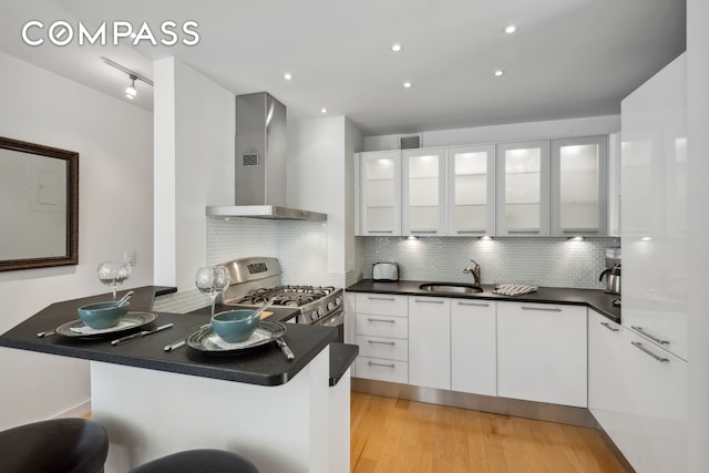 kitchen with wall chimney exhaust hood, a breakfast bar, kitchen peninsula, and white cabinets