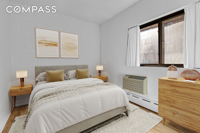 bedroom with a wall mounted air conditioner, baseboard heating, light wood-type flooring, and brick wall