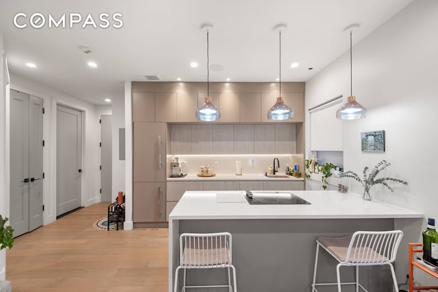 kitchen featuring kitchen peninsula, a breakfast bar area, pendant lighting, gray cabinets, and light hardwood / wood-style floors