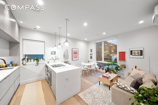 kitchen with kitchen peninsula, light wood-type flooring, a wall mounted air conditioner, sink, and decorative light fixtures