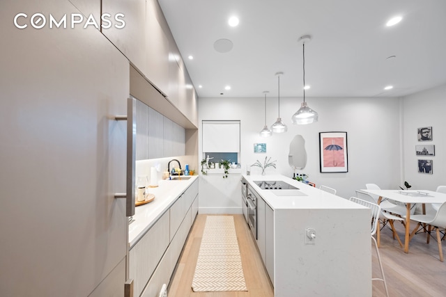 kitchen with sink, kitchen peninsula, decorative light fixtures, and light wood-type flooring