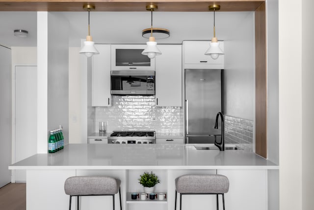 kitchen with a kitchen bar, stainless steel appliances, white cabinetry, and hanging light fixtures