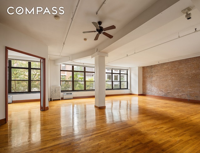 unfurnished room with ceiling fan, light hardwood / wood-style floors, radiator, and brick wall