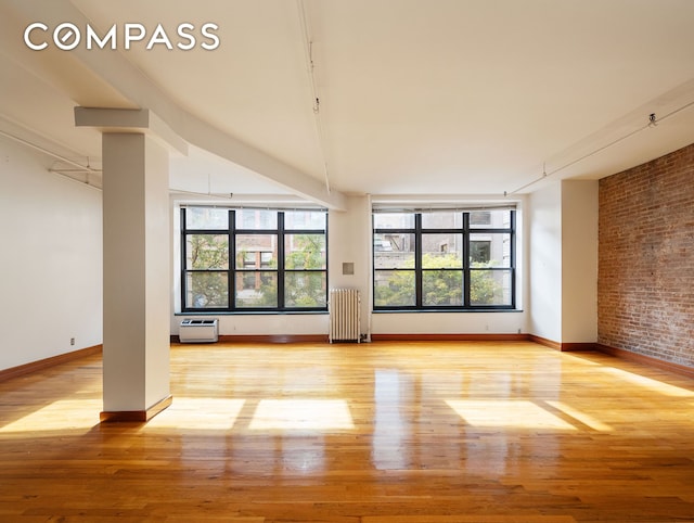 unfurnished living room with a wealth of natural light, radiator heating unit, and light hardwood / wood-style floors