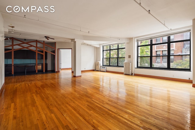 unfurnished living room with radiator, ceiling fan, light hardwood / wood-style flooring, and plenty of natural light