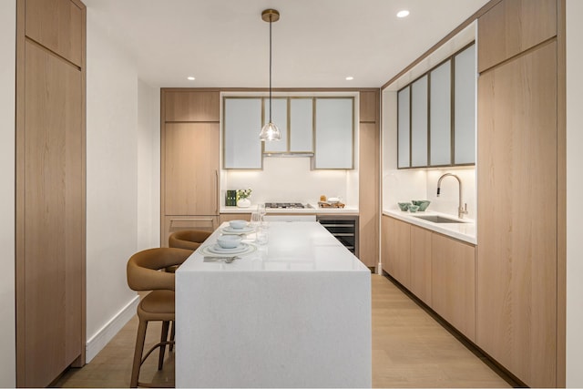 kitchen featuring a kitchen breakfast bar, sink, hanging light fixtures, light wood-type flooring, and a kitchen island